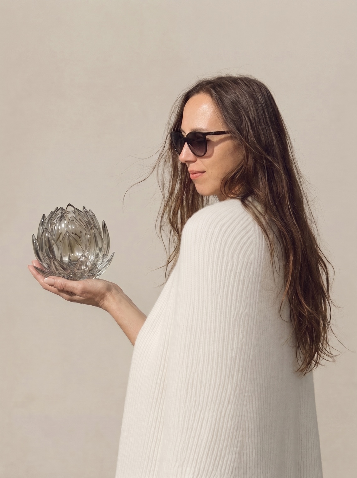 Woman in sunglasses and an ivory wrap holding a glass artichoke